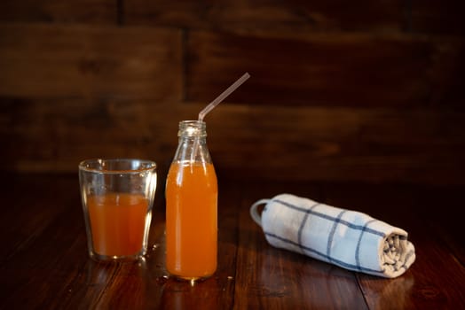 vintage bottle with juice, straw, and towel on wooden table.