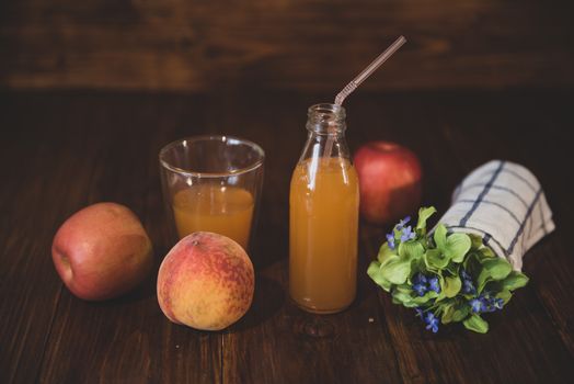 Fresh juice in bottle on wooden table with flowers and fruits