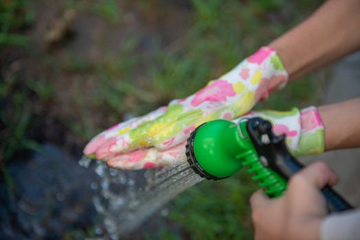 Women's hands in garden gloves are washed from a hose.