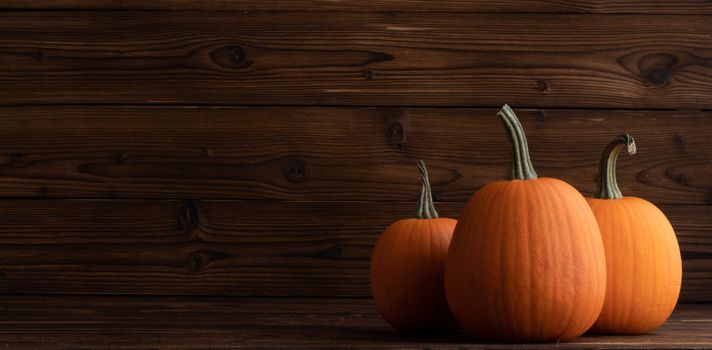 Three orange pumpkins on dark wooden background , Halloween concept , copy space for text
