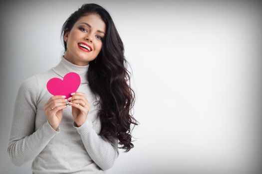 Beautiful young brunette woman holding pink paper heart , looking at camera