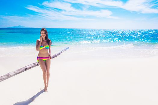 Happy tanned girl in rainbow bikini at seaside, blue sea water in background