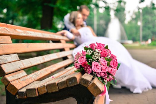 bouquet on wooden bench with bride and groom in the background, focus on the flowers. flowers on the background of the newlyweds