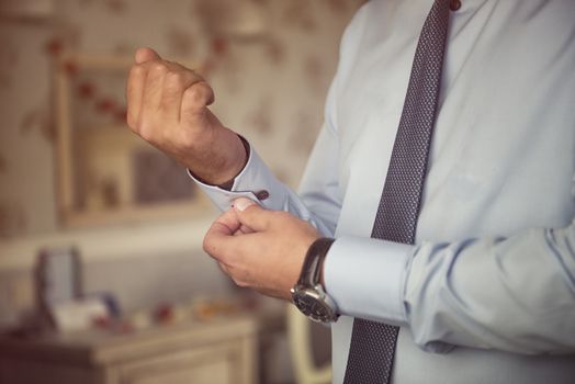 Male hands fixing stylish silver cufflinks on white shirt cuffs sleeves in formal suit with elegant buttons