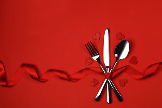 Love, romance, Valentine's day concept - festive table setting cutlery and decorative hearts on red background