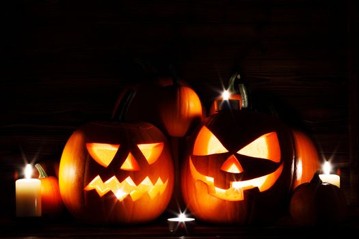 Three Halloween pumpkins head jack o lantern and candles on wooden table background