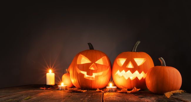 Three Halloween pumpkins head jack o lantern and candles on wooden table background