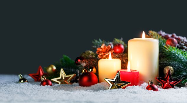 Burning christmas candles with red and golden decorative stars , baubles , pine cones and green branches on snow
