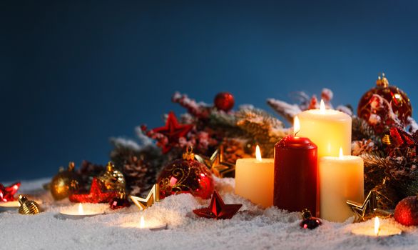 Burning christmas candles with red and golden decorative stars , baubles , pine cones and green branches on snow