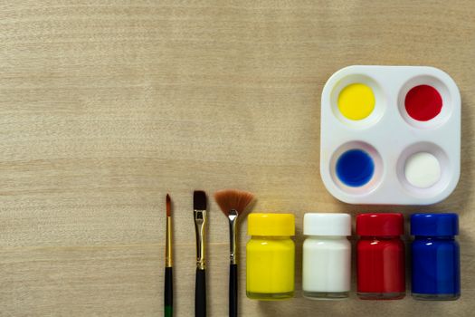 Palette and poster color bottle with paint brush on wooden table background. Top view and copy space.