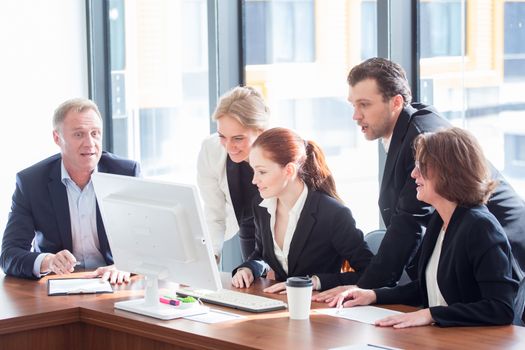 Business team look at one computer monitor having discussion in office