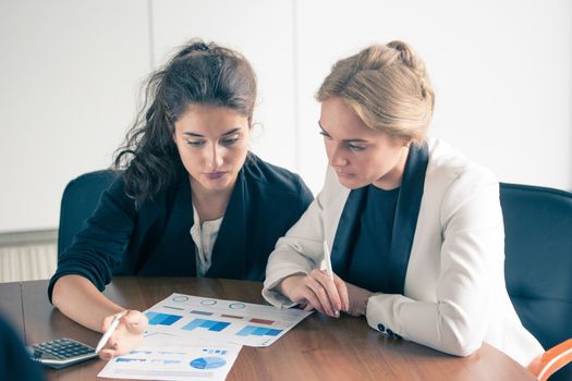 Business women pointing at diagrams discussing financial reports at workplace