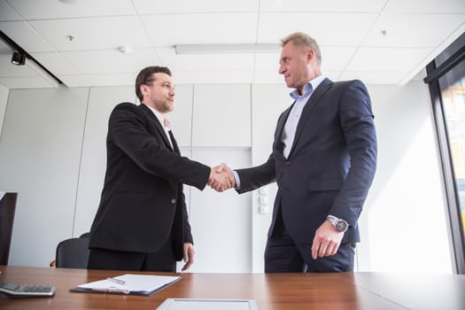 Business people in formal wear sign contract and shaking hands