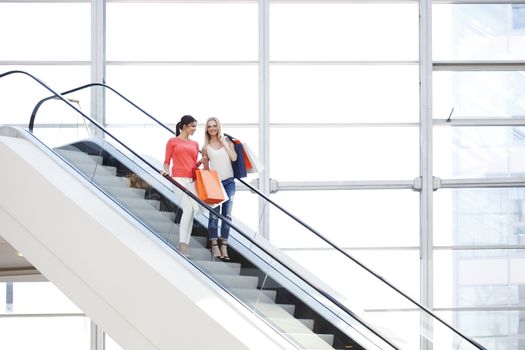 Young beautiful happy women on escalator of shopping mall