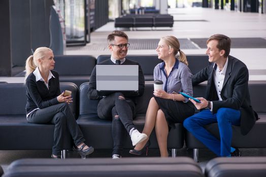 Portrait of happy business people talking at break in business center lobby sitting together at sofa