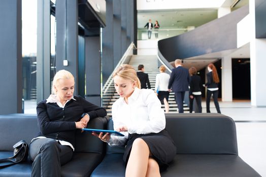 Business women sitting in lobby and surfing the net with tablet pc