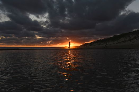 Silhouette of a woman in the sunset over tide pool water surface, Mossel Bay, South Africa