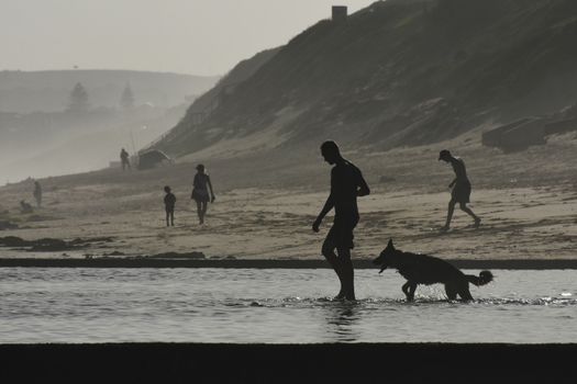 A man and his canine companion heads out for a refreshing beach tide pool swim, Mossel Bay, South Africa