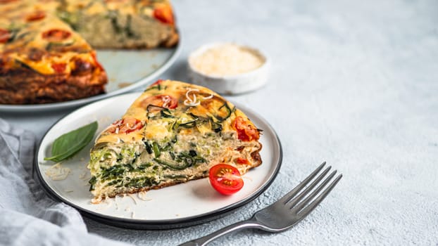 Zucchini pie and ingredients on gray background, copy space. Piece of delicious savory pie with zucchini, tomatoes, herbs and cheese. Idea and recipe for healthy baking and lot to harvest of zucchini