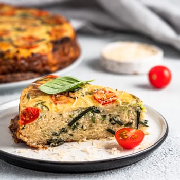 Zucchini pie and ingredients on gray background, copy space. Piece of delicious savory pie with zucchini, tomatoes, herbs and cheese. Idea and recipe for healthy baking and lot to harvest of zucchini