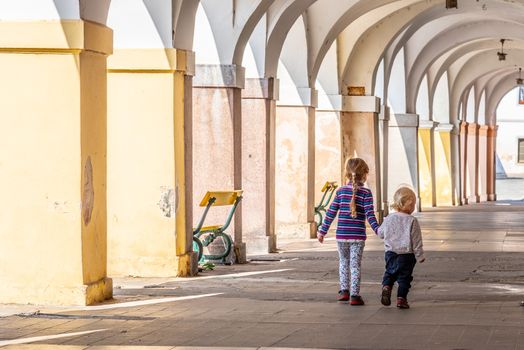 Two young children walk together hand in hand in the old town arcade street. Family love and friendship theme.
