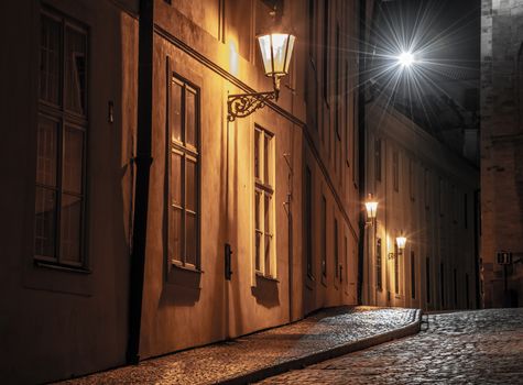 Narrow cobbled street illuminated by street lamps of Old Town, Prague, Czech Republic.