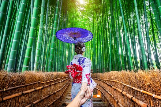 woman wearing japanese traditional kimono holding man's hand and leading him to Bamboo Forest in Kyoto, Japan.