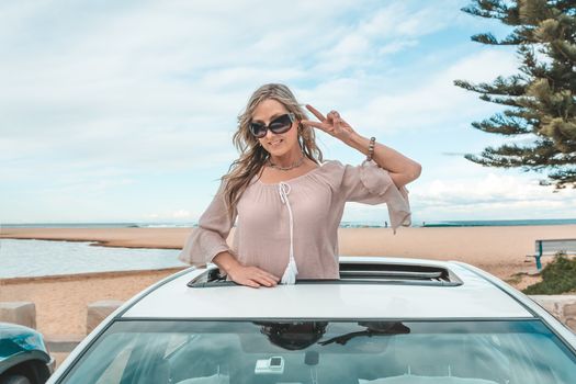 Fun loving woman enjoy travelling places in her car, she is standing in the sky roof of her car at the beach