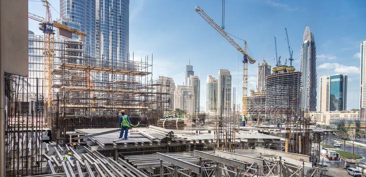 Laborers working on modern constraction site works in Dubai. Fast urban development consept.