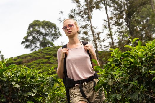 Active caucasian blonde woman enjoing fresh air and pristine nature while tracking among tea plantaitons near Ella, Sri Lanka. Bacpecking outdoors tourist adventure.