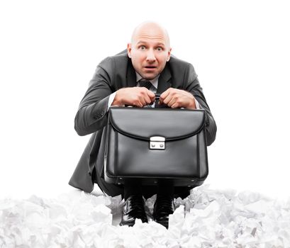 Business problems and failure at work concept - unhappy scared or terrified businessman in depression hand holding briefcase sitting down floor on crumpled torn paper document heap white isolated