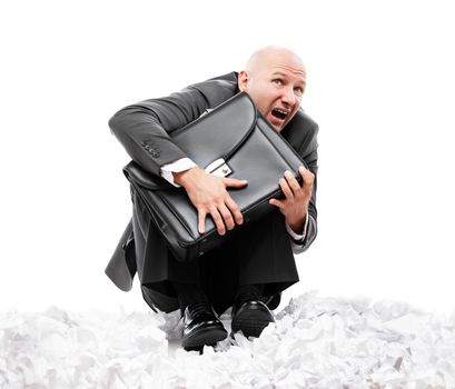 Business problems and failure at work concept - unhappy scared or terrified businessman in depression hand holding briefcase sitting down floor on crumpled torn paper document heap white isolated