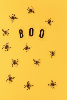 Halloween holiday flat lay. Spiders and inscription Boo on orange background. Minimal style. Vertical. Trick-or-treat concept.