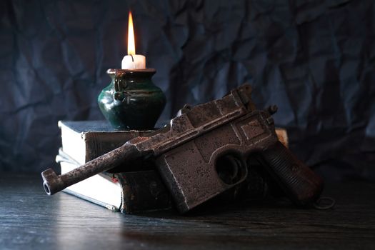 Still life with old military handgun near ancient books and candle