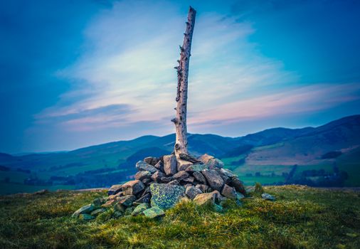 Scottish Hilltop With Cairn And Wooden Post At Sunset