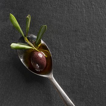 A black olive in the spoon with a black sytone