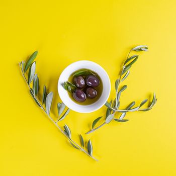 Olive oil and olives on a yellow surface with some Olive branches