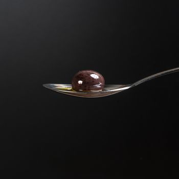 A black olive in the spoon with a black background