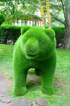 The figure of a bear standing on four legs in a green Park.