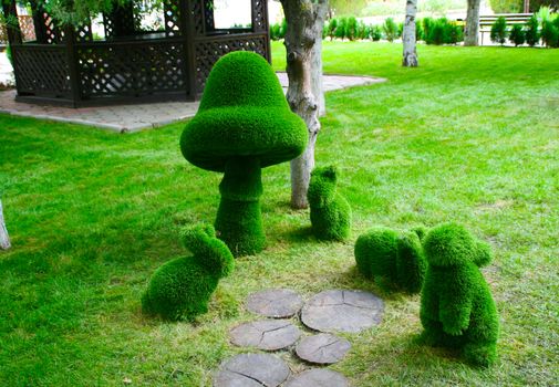 Sculptures of hares and mushrooms in different positions in the Park green on the background of trees.