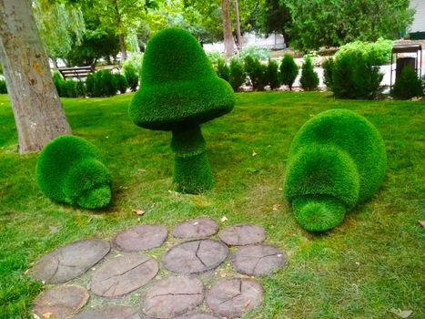 
Sculptures of two hedgehogs and a fungus between them in the Park are green against the background of trees.

