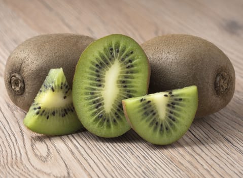 Ripe juicy kiwi fruit with sliced segments on wooden background.