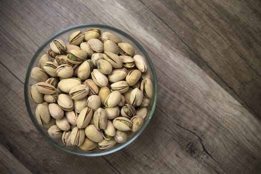 Glass bowl of pistachios on a wooden table as background
