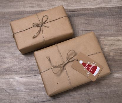 Christmas or New Year gift boxes wrapped in kraft paper with blank gift tag on old wooden background.