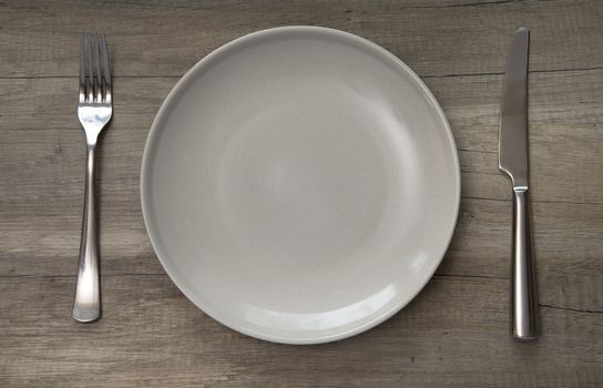 Ceramic plate, fork and knife on wooden planks table
