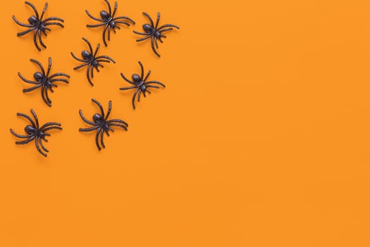 Halloween flat lay. Black spiders on orange background with copy space. Minimal style. Horizontal. Trick-or-treat concept.