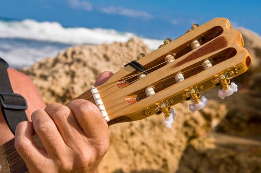 Guitar neck and hand on strings, a man plays on the shor of the Mediterranean Sea