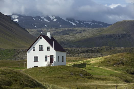 Lonely house standing on rock at the bottom of mountain, Iceland.