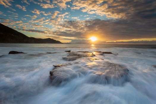 Tidal waves cascade over the weathered rocks of the outer rockshelf on the southern end of the beach as the sun rises. Location: Coalcliff Australia