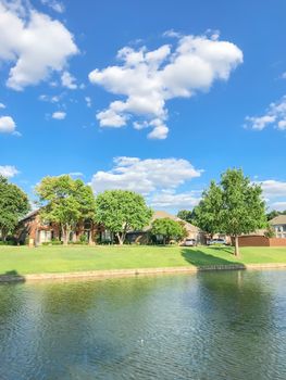 Beautiful waterfront house with row of mature bold cypress trees in suburbs Dallas, Texas, USA. Suburban single family detached home along river with high stone retaining wall, green grass lawn